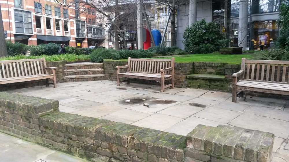 Image shows three benches within a walled area, with a raised grassy area beyond